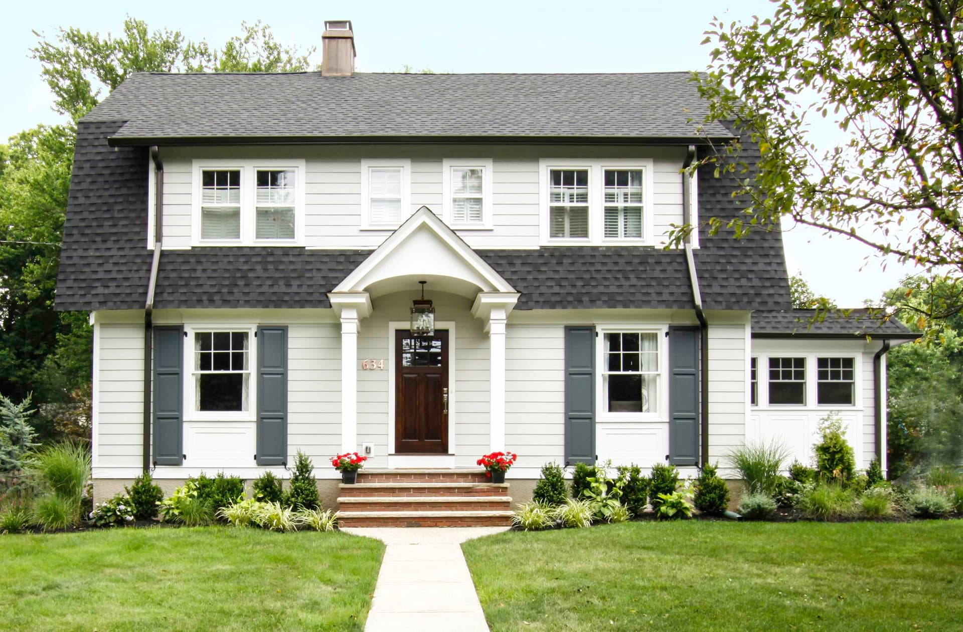 Front elevation of a white clapboard Dutch Colonial with a gambrel roof, dark gray shutters and an arched portico in Westfield, NJ