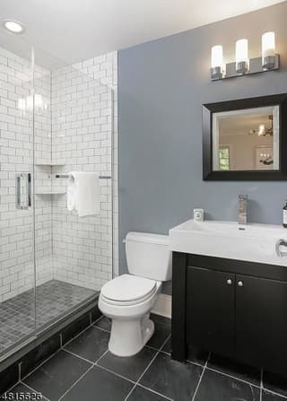 Guest bathroom of a Westfield, NJ coastal colonial renovation, with a subway-tiled shower, a dark vanity and slate tile underfoot
