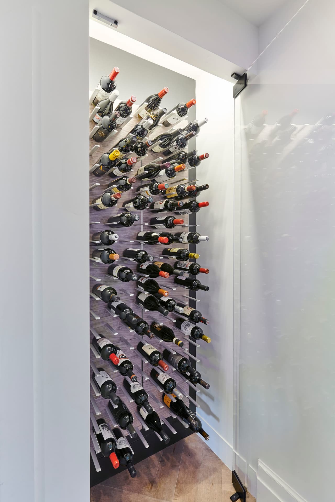 Wine wall with bottles stored on metal pegs floor to ceiling, beside a glass door