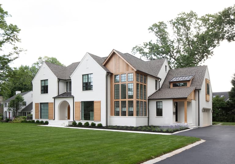 Front of a white painted brick custom home in Westfield, NJ, with cedar accents, a steep gabled window bay and an arched entry, built by Michael Robert Construction
