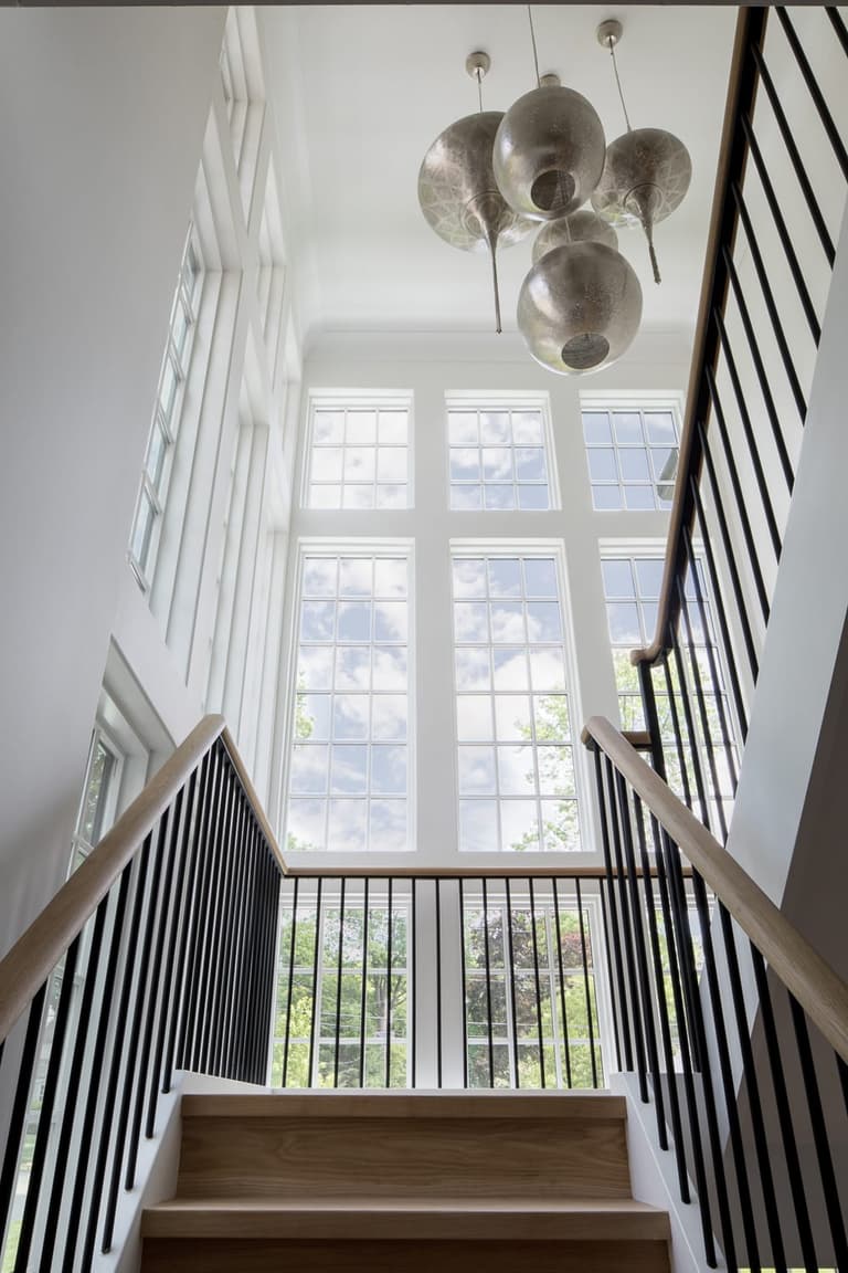 Stairwell of a Westfield, NJ custom home, with oak treads, a slim black railing and a cluster of alabaster globe pendants by the tall window