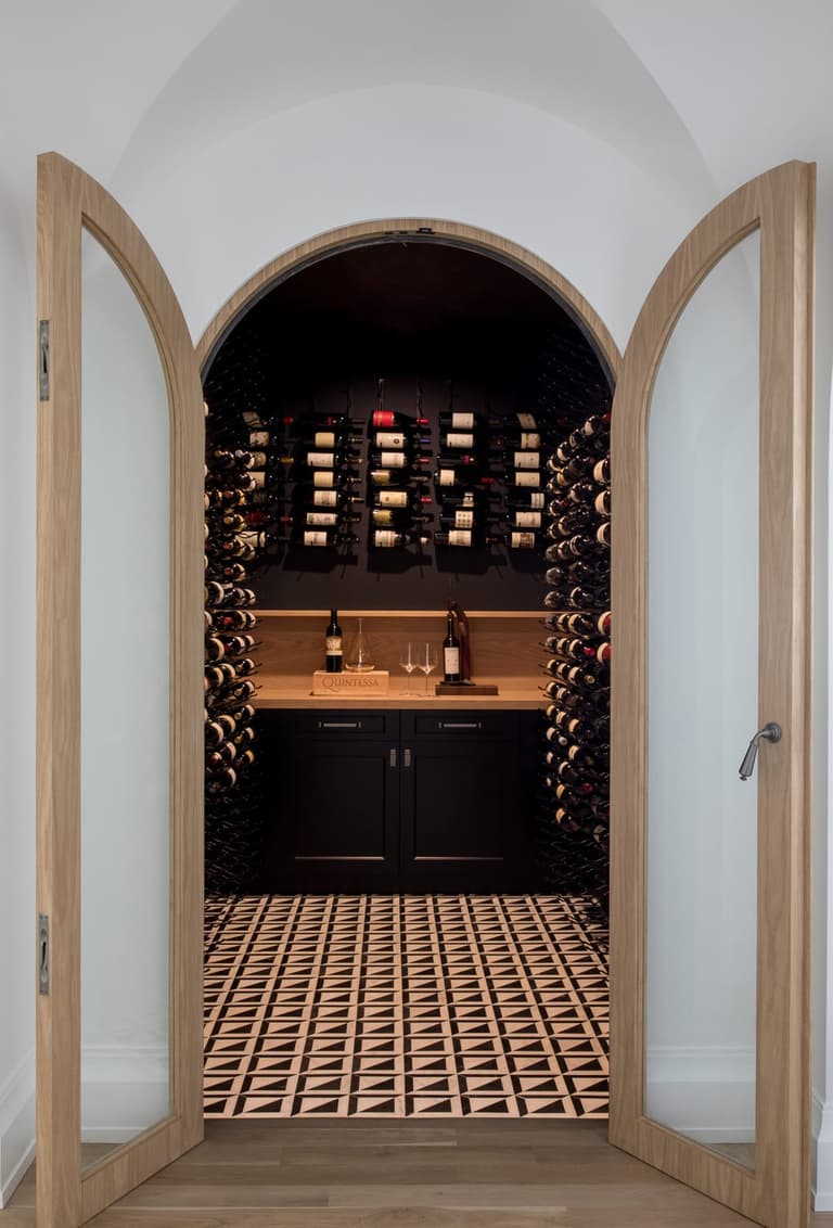 Arched white oak doors opening onto a wine room with black cabinetry and patterned tile, in a Westfield, NJ new home