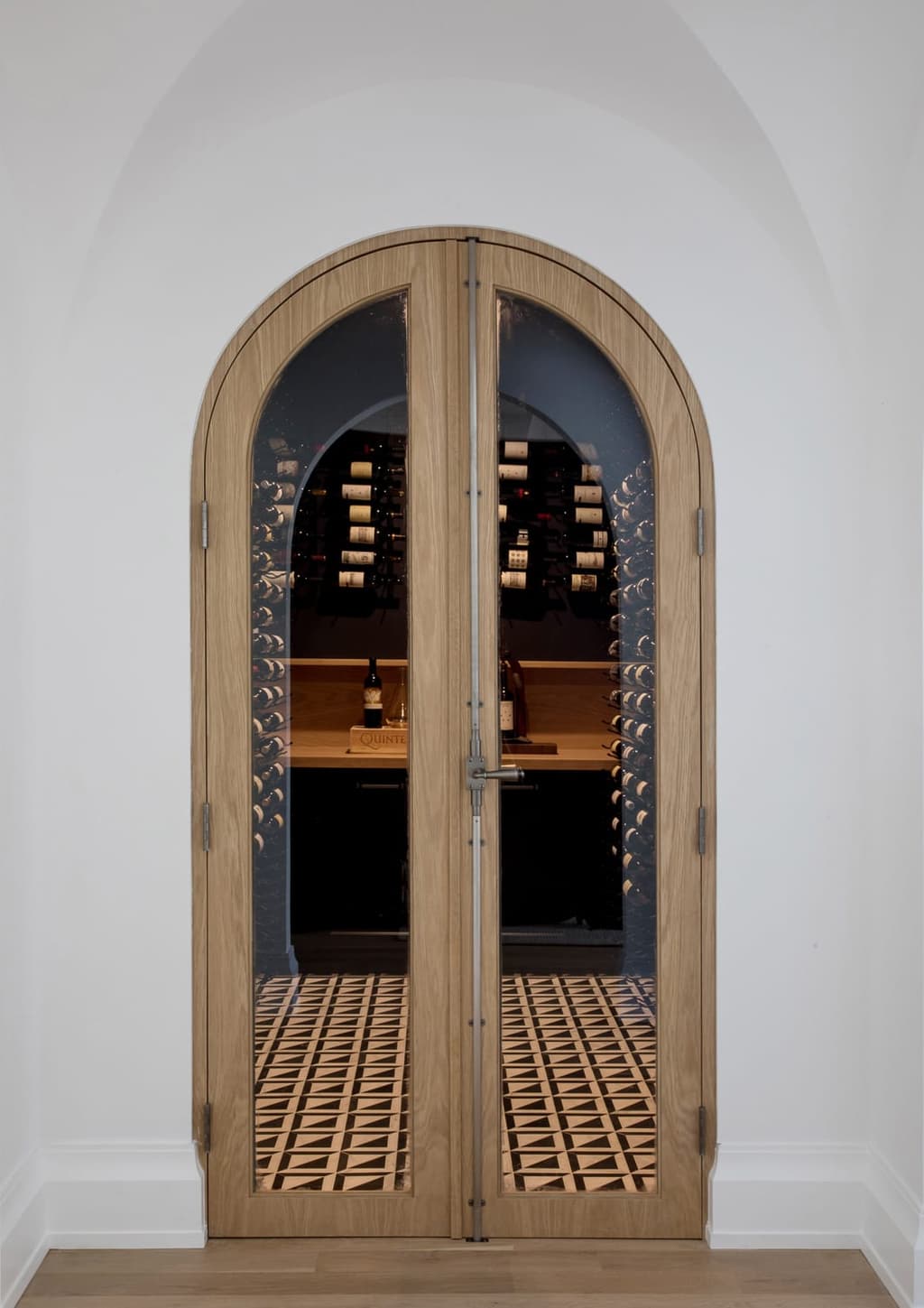 Arched glazed oak doors on the wine room of a Westfield, NJ new-construction home, set into a plaster surround