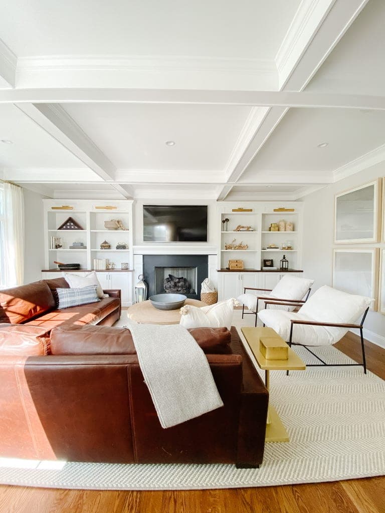Family room under a coffered ceiling with a cognac leather sofa, white built-ins and a fireplace