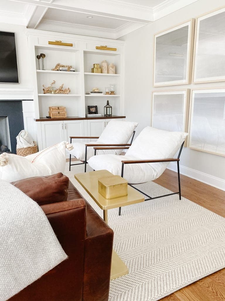 Family room corner with white built-in shelving, framed art and a pair of sling chairs
