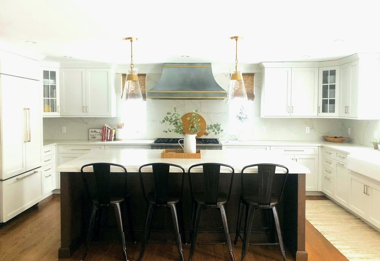 Kitchen with a dark island, black counter stools, brass sconces and a pale plaster range hood