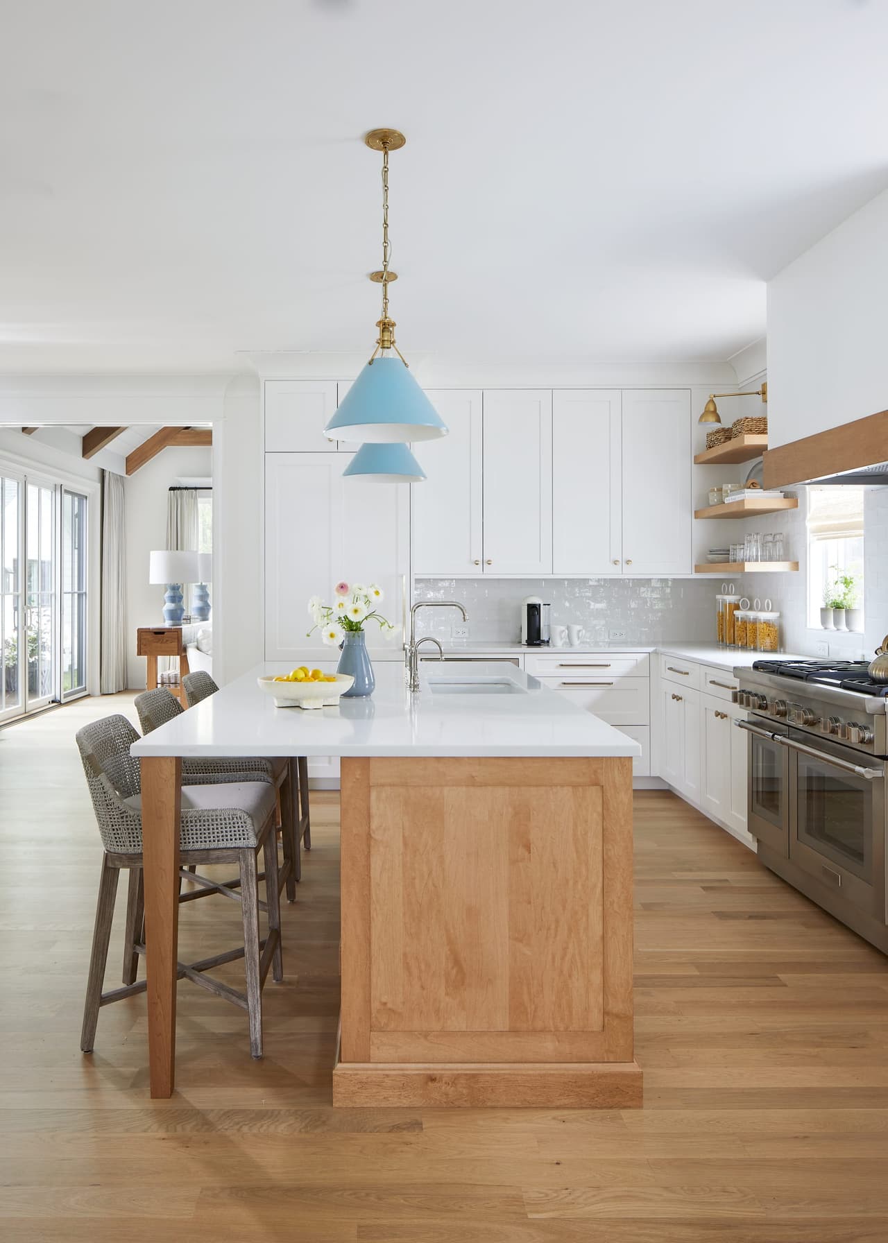 Kitchen looking toward the stainless range, with a white oak island, two pale blue pendants and open shelving