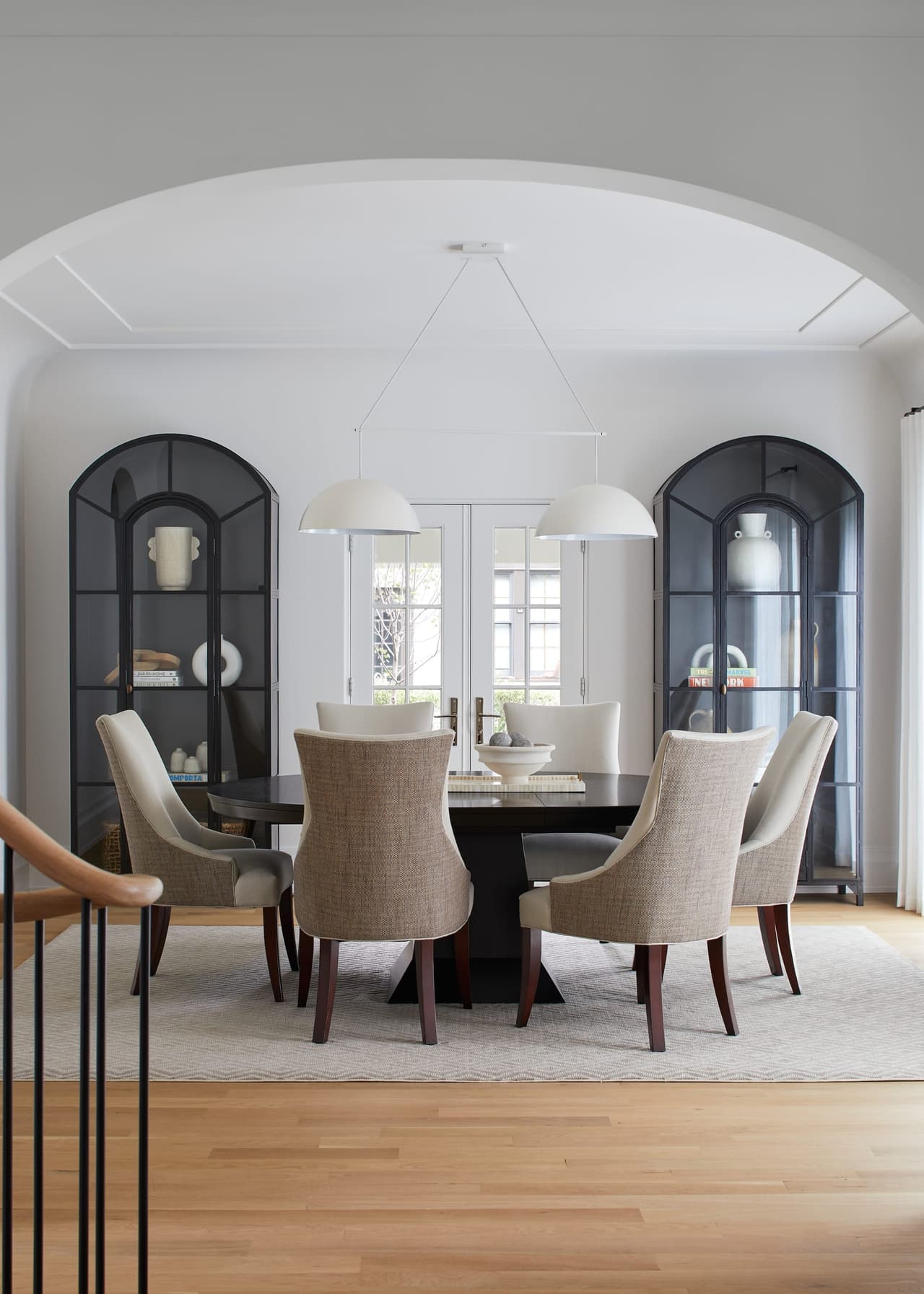 Dining room with arched glass-front cabinets, a round table, upholstered chairs and paired pendants