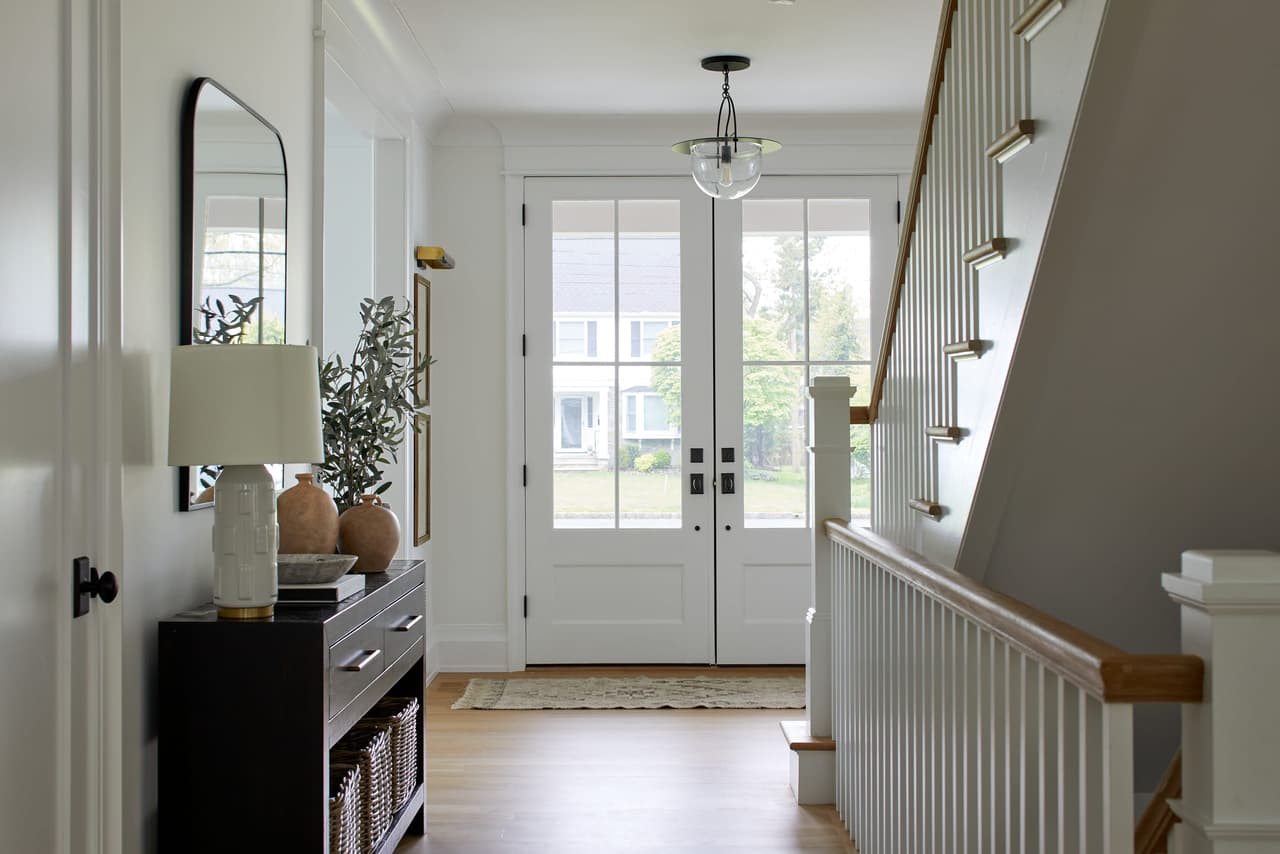 Entry hall with a glass front door, a white-risered stair with oak treads, a dark console and an arched mirror