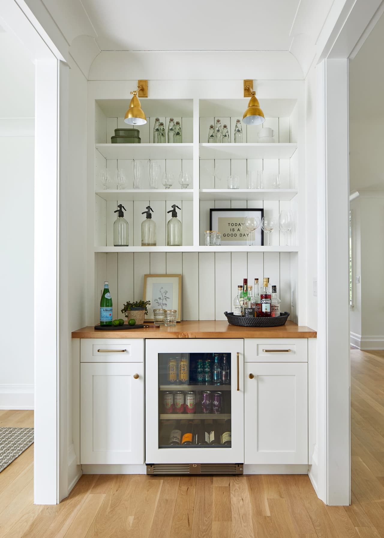 Bar alcove with white cabinetry, lit glass shelving, a butcher-block counter and a glass-front beverage refrigerator