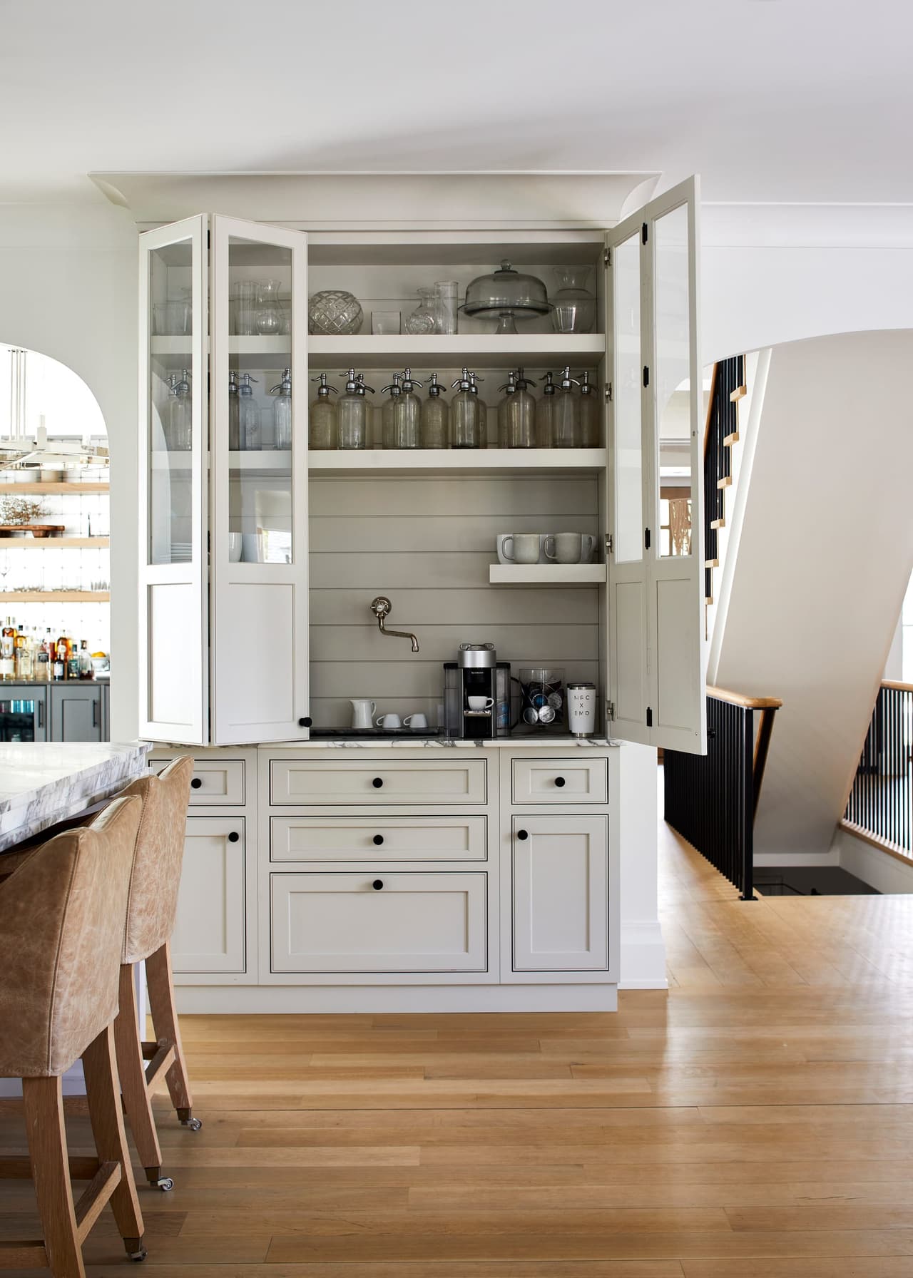 Coffee station in a glass-front cabinet with a marble counter, beside the kitchen island