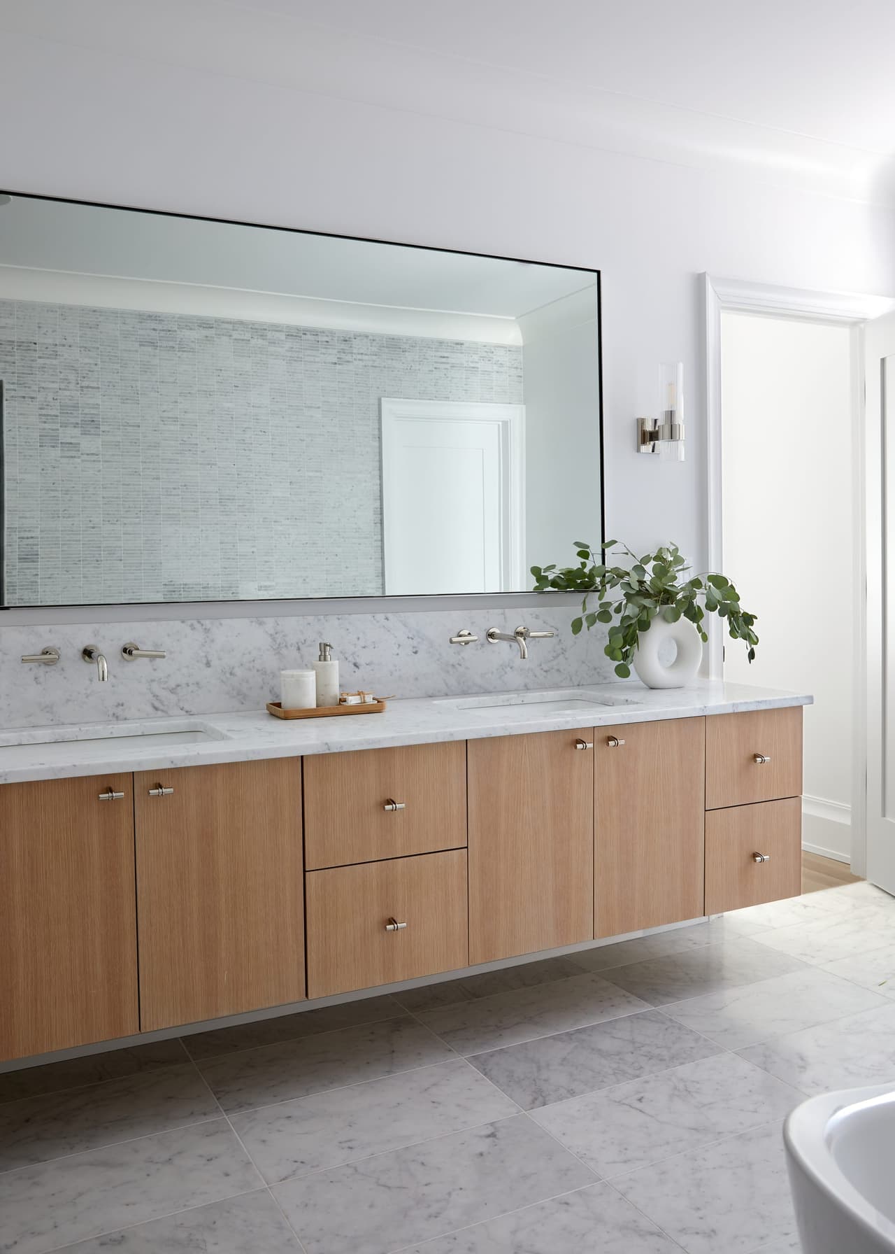 Primary bathroom with a white oak floating double vanity, a full-width mirror and a freestanding tub