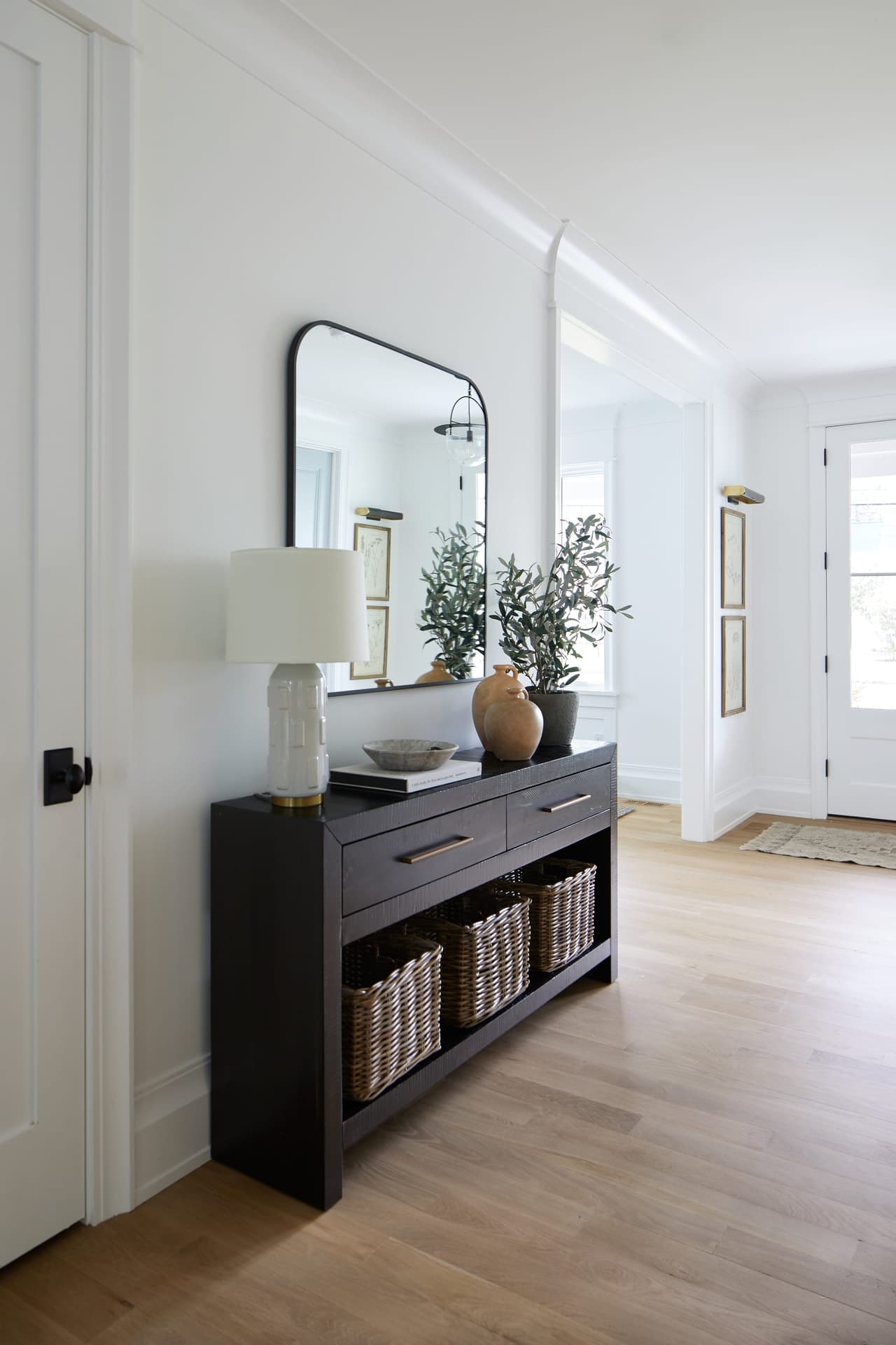 Entry hall of a Westfield, NJ new-construction home, with a dark console under an arched mirror and a lamp, and baskets on the shelf below