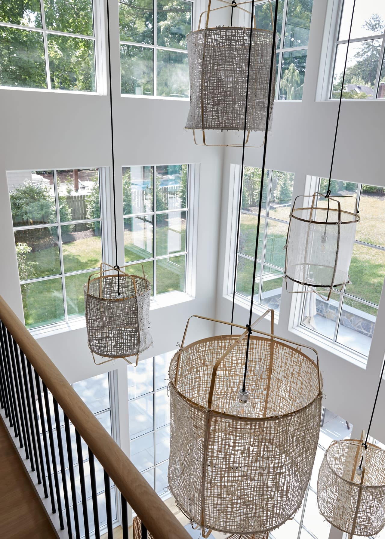 Woven lanterns hung at three heights in the double-height window wall of a Westfield, NJ renovation and addition, seen from the landing