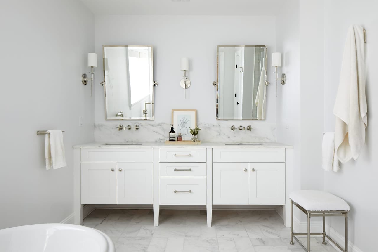 Primary bathroom with a double vanity, two framed mirrors between sconces and a freestanding tub on marble tile
