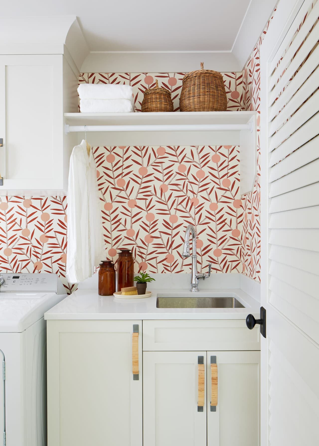Laundry room with coral patterned wallpaper, shiplap, a utility sink and woven baskets on the shelf above