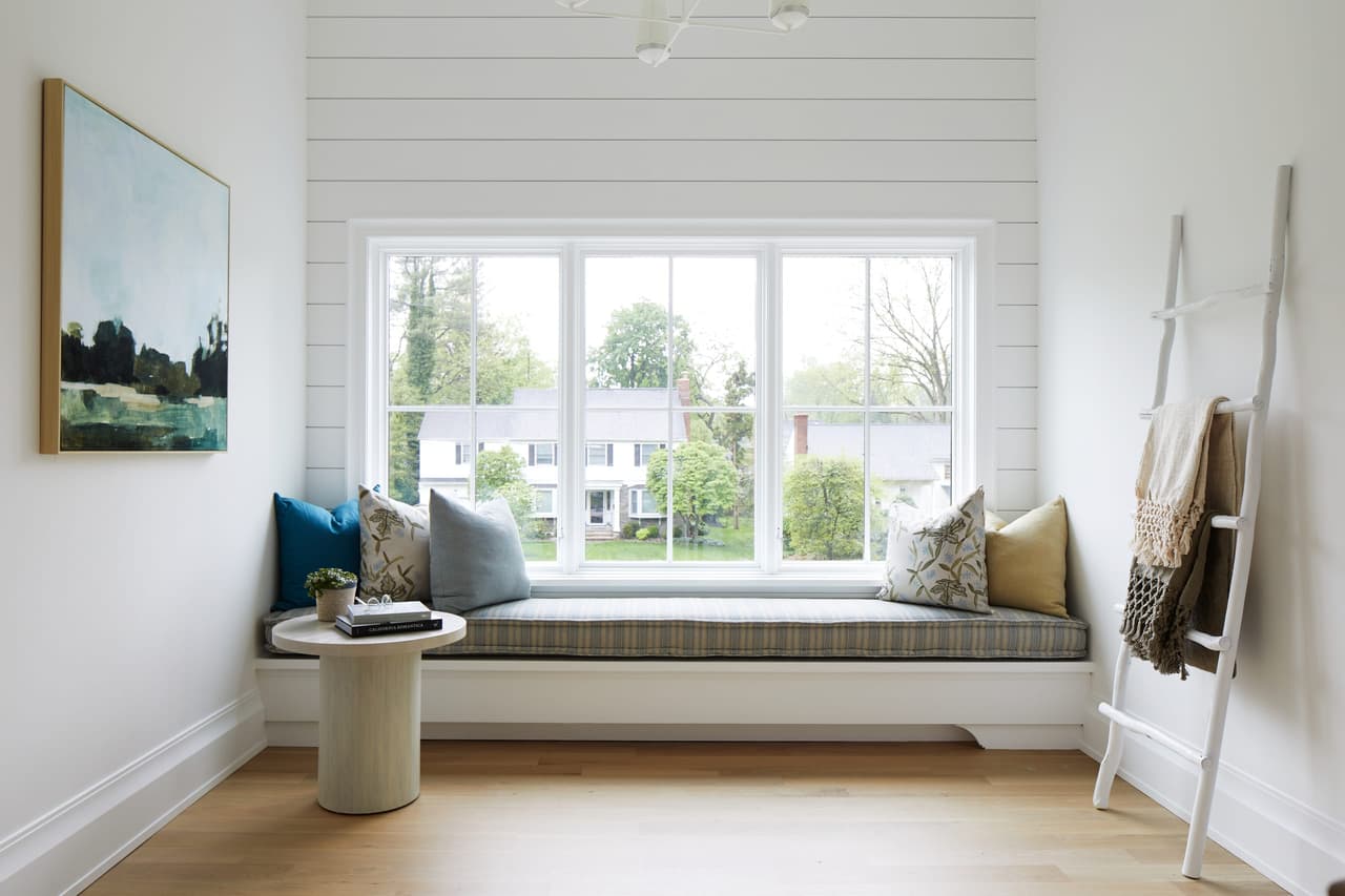 Window seat on the upstairs landing, with shiplap walls, a ladder blanket rail and a view over the front lawn