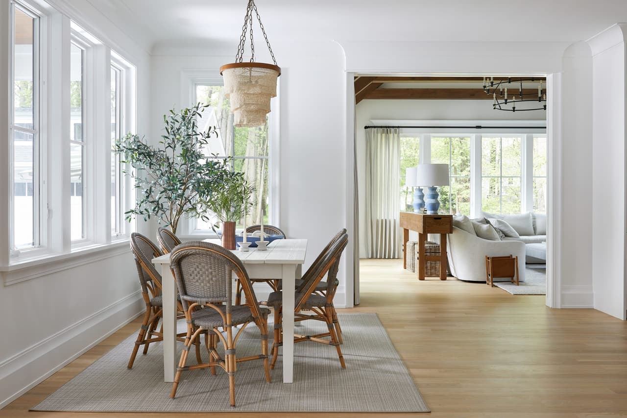 Dining area with rattan bistro chairs under a woven pendant, looking through to the living room beyond