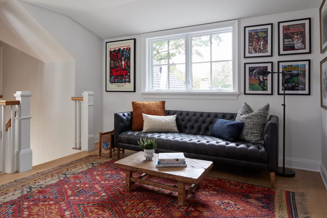 Attic office in a Westfield, NJ custom home, with a tufted leather sofa, a gallery wall of framed prints and a patterned red rug under a sloped ceiling