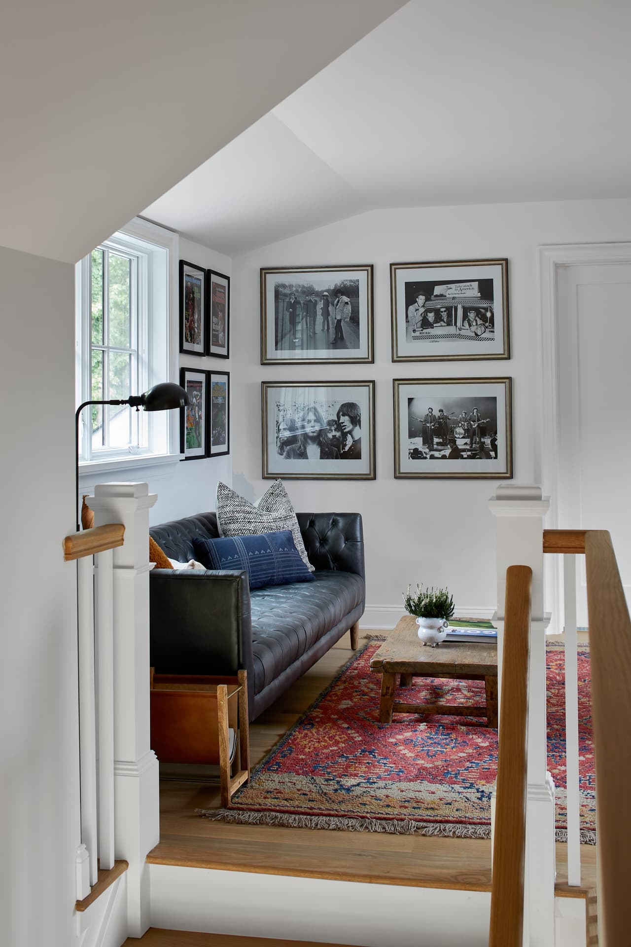 Attic sitting area in a Westfield, NJ custom home, with a tufted leather sofa under a gallery wall and a swing-arm sconce beside the stair rail