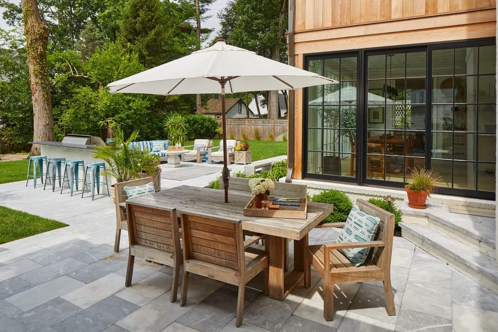 Backyard dining table under an umbrella on the bluestone terrace of a Westfield, NJ new-construction home, beside sliding glass doors into the house