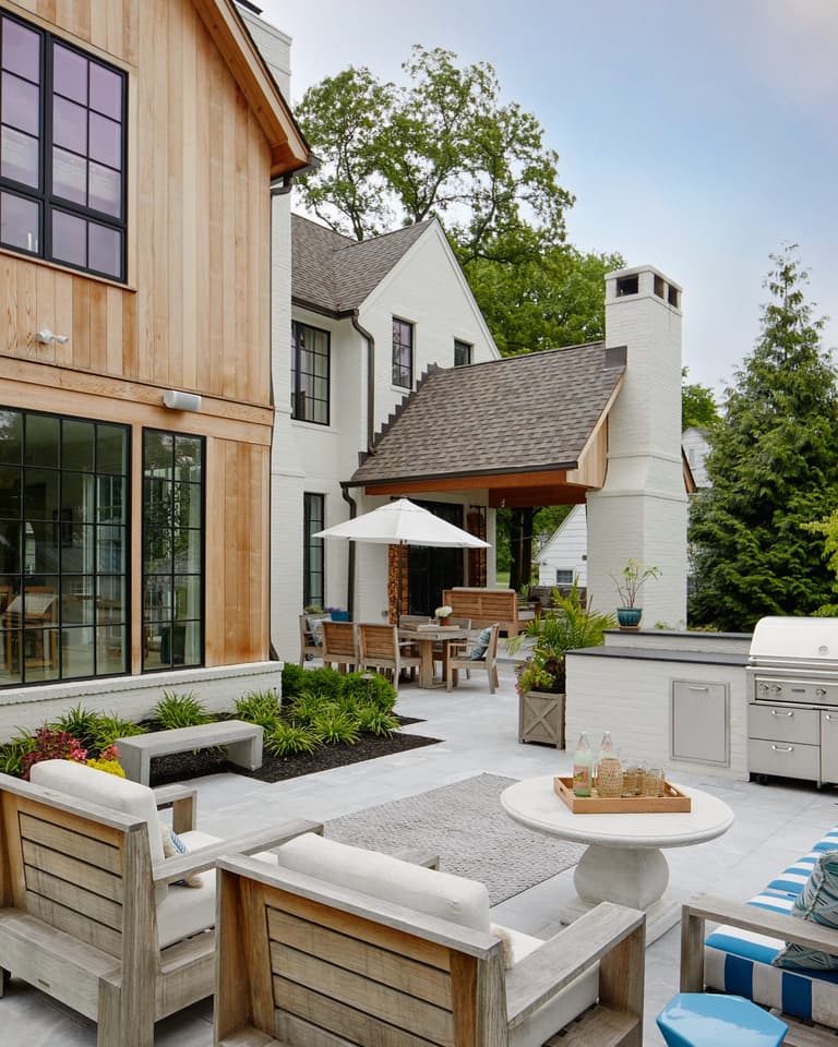 Backyard terrace with a built-in outdoor kitchen, teak seating, planters and an umbrella beside a new construction home in Westfield, NJ