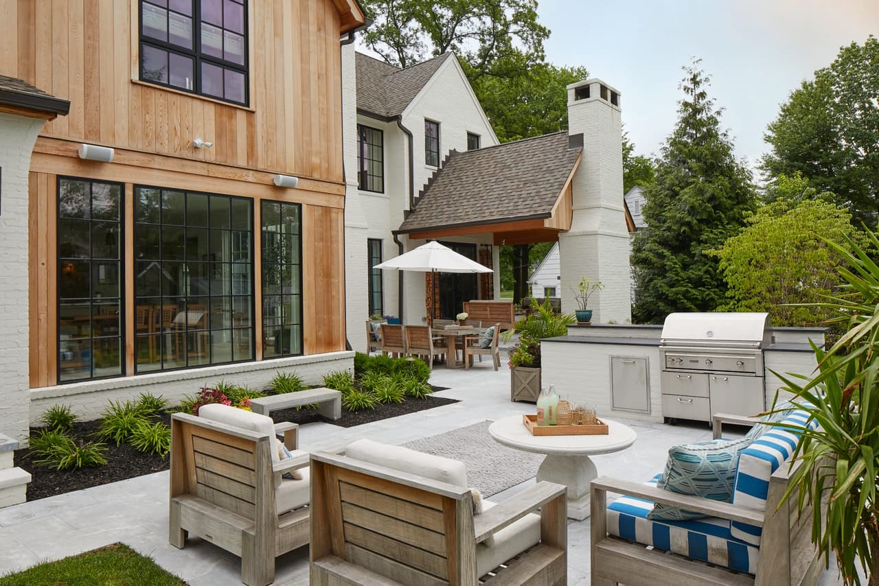 Backyard entertaining space with a built-in grill, teak seating and an umbrella beside a new construction home in Westfield, NJ