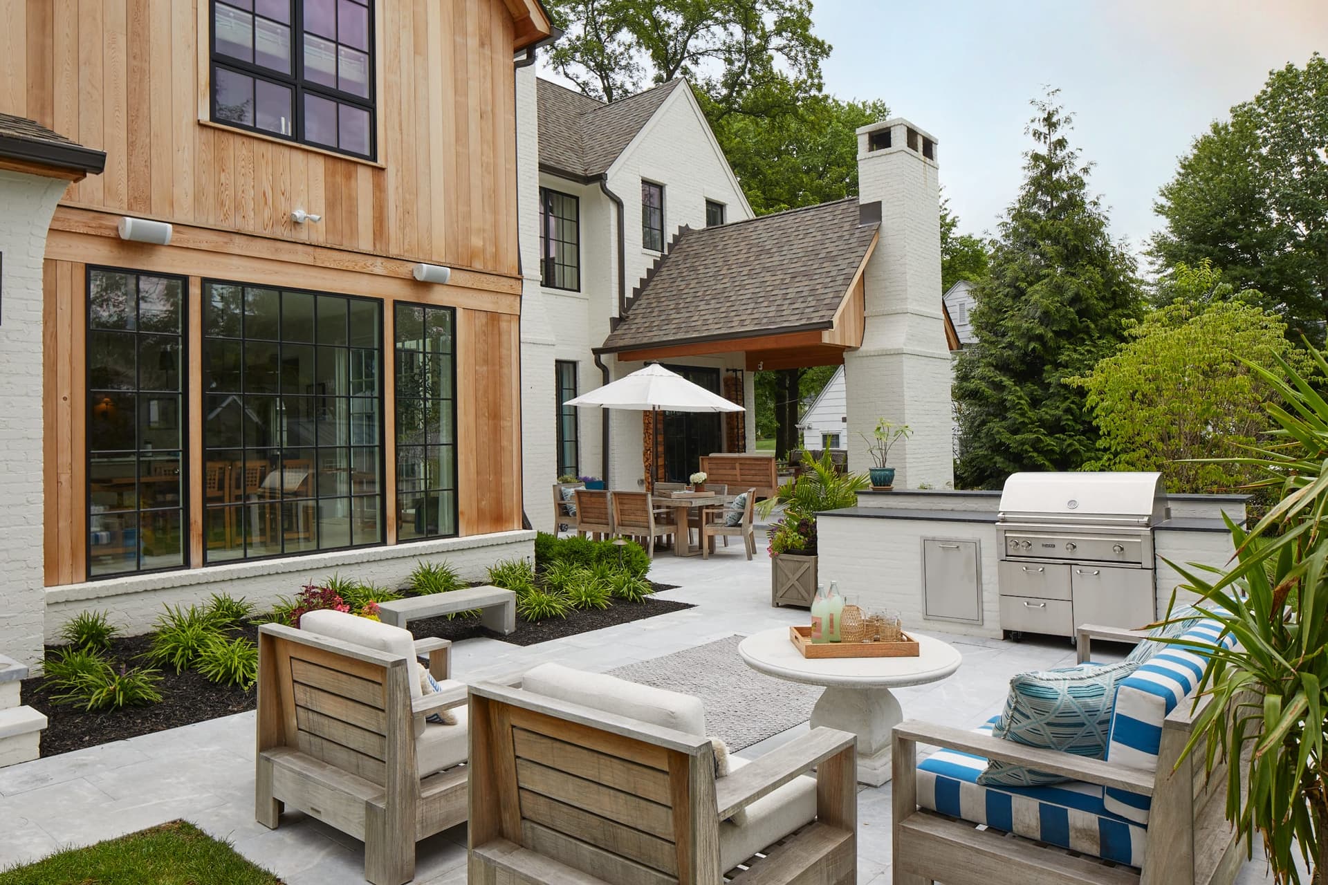 Backyard entertaining space with a built-in grill, teak seating and an umbrella beside a new construction home in Westfield, NJ