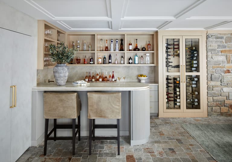 Family room bar in a Westfield, NJ renovation, with a coffered ceiling, open shelving, glass-front wine storage and a stone-clad counter with black stools