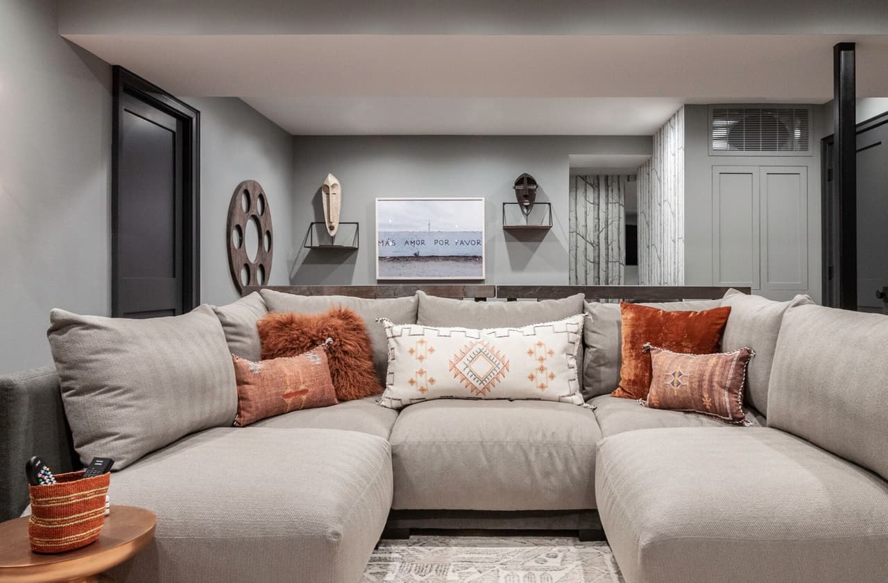 Basement media room in a Westfield, NJ renovation, with a deep sectional, terracotta cushions and a wall-mounted television between shelf-mounted objects