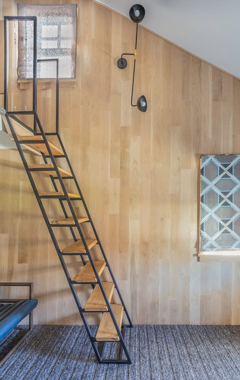 Ship's ladder in black metal and oak rising to a loft bed against a wood-paneled wall in a Westfield, NJ bedroom remodel