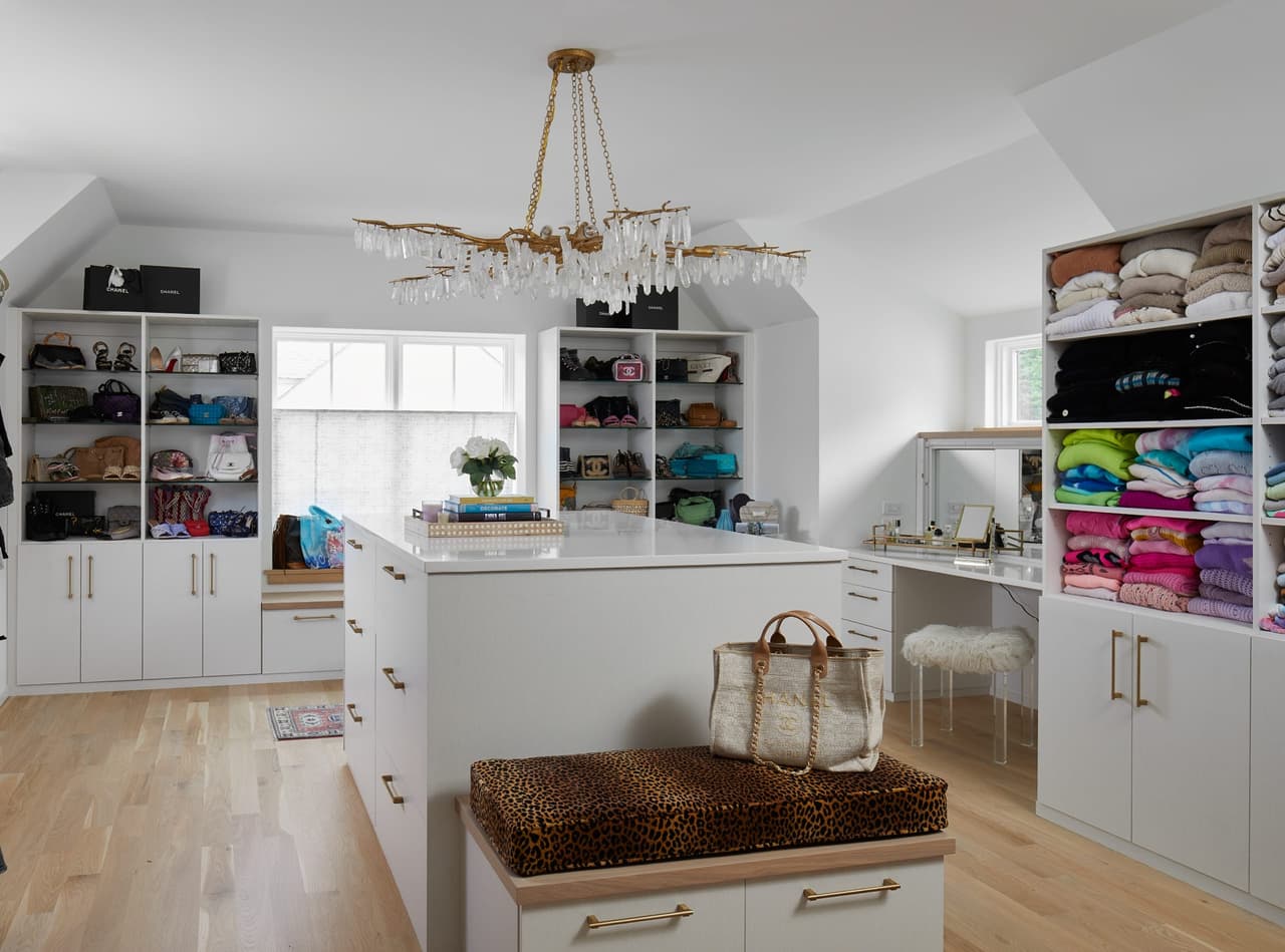 Walk-in closet in a Westfield, NJ custom home, with white built-in cabinetry, a brass chandelier and a leather-topped island under a sloped ceiling