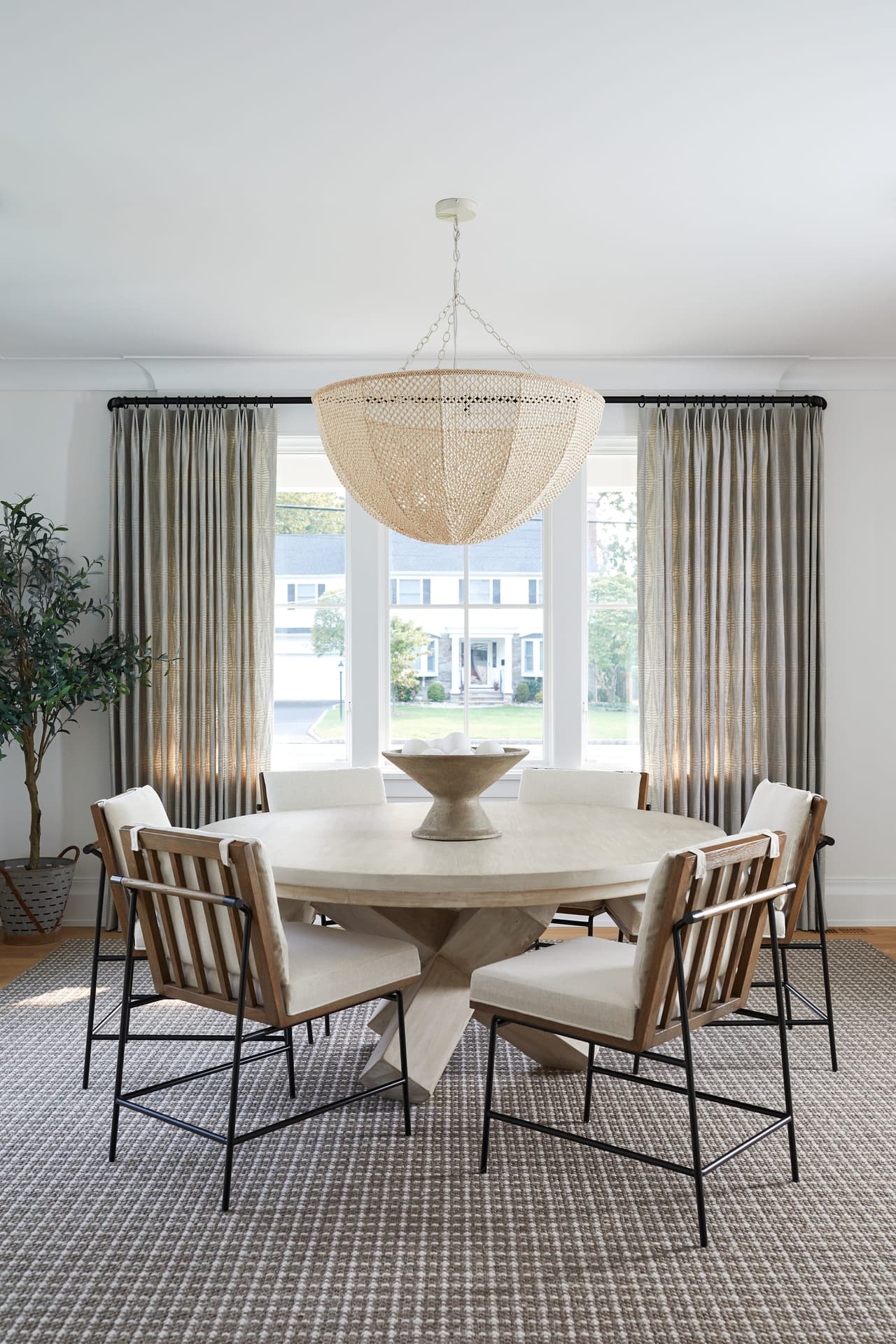 Dining room in a Westfield, NJ new-construction home, with a beaded chandelier over a round table, cane chairs and linen curtains