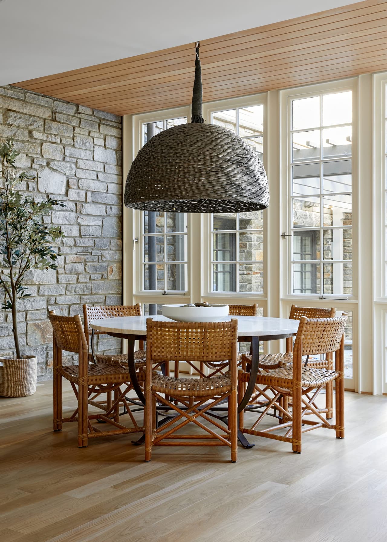 Eat-in kitchen area in a Westfield, NJ renovation, with a stone wall, a planked ceiling, a hammered metal pendant and cane chairs at a round table