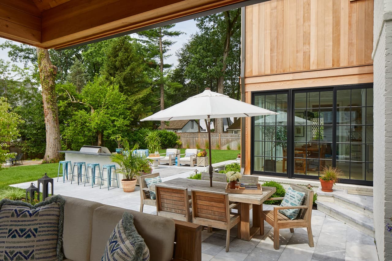 Entertaining backyard of a Westfield, NJ new-construction home, with a cedar-clad outdoor kitchen, teak seating and an umbrella on the terrace