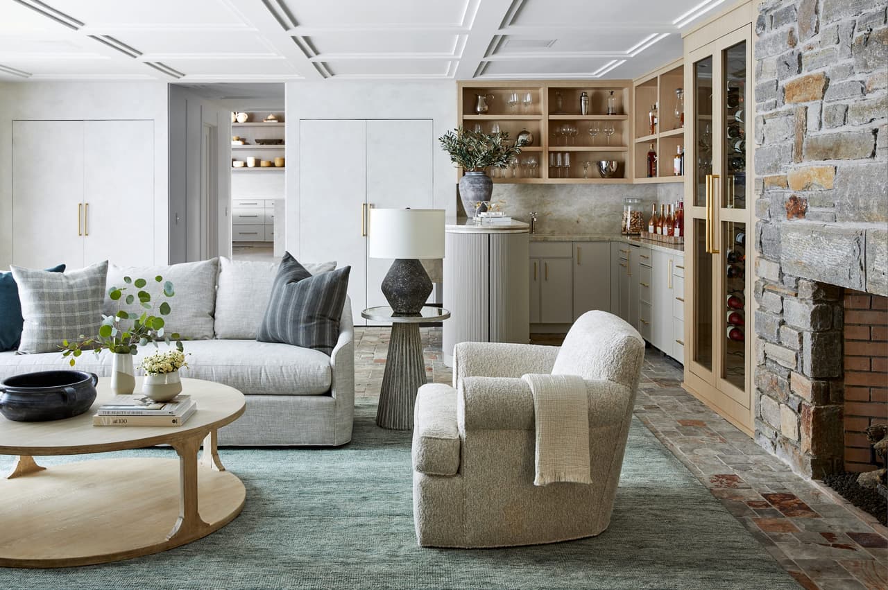 Family room of a Westfield, NJ home renovation with a coffered ceiling, a stone fireplace wall and a built-in bar with glass-front cabinets at the far end