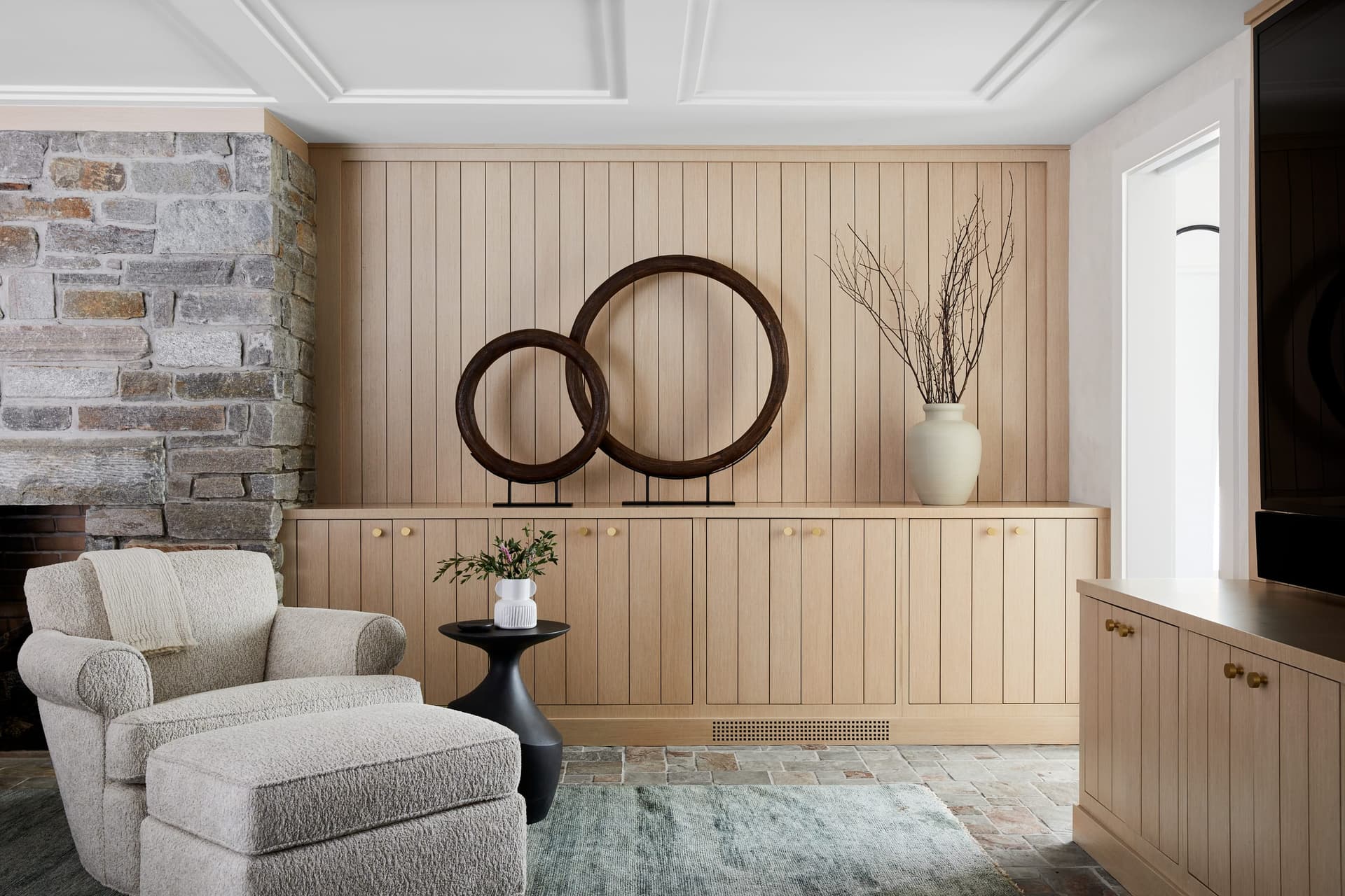 Vertical oak planking and low custom built-ins along the wall of a Westfield, NJ family room renovation, beside an exposed stone chimney breast