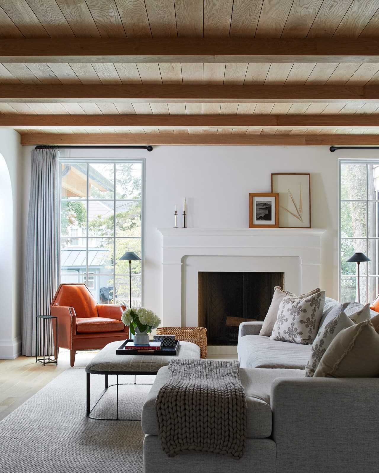 Family room of a Westfield, NJ custom home with a white fireplace between windows, a plank ceiling on a painted beam and a rust leather chair beside the sofa