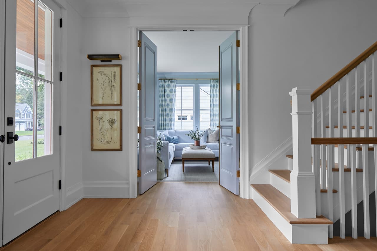 Entry of a Westfield, NJ new-construction home with white oak floors, a glazed front door, a painted stair with turned newel and a sitting room through the doorway