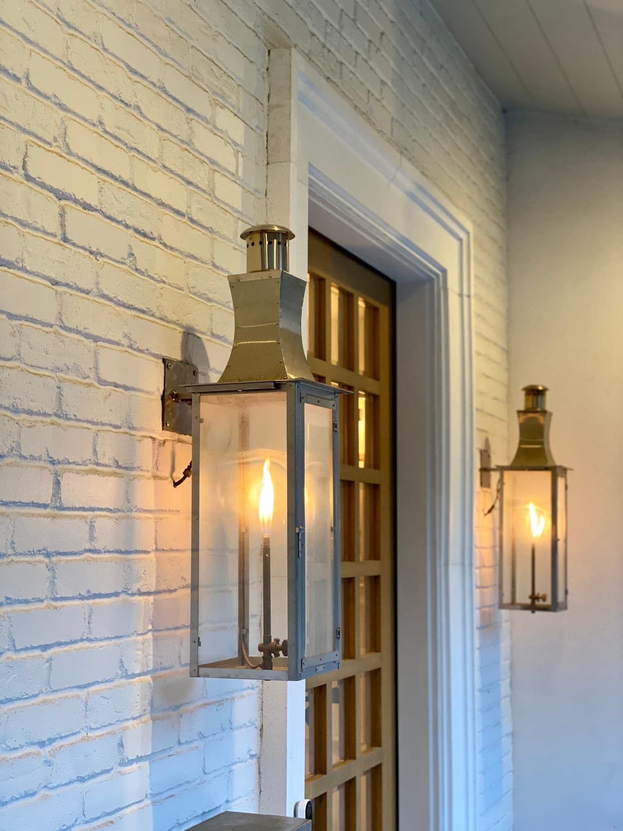 Pair of brass gas lanterns lit either side of a doorway on the painted brick of a Westfield, NJ new-construction home