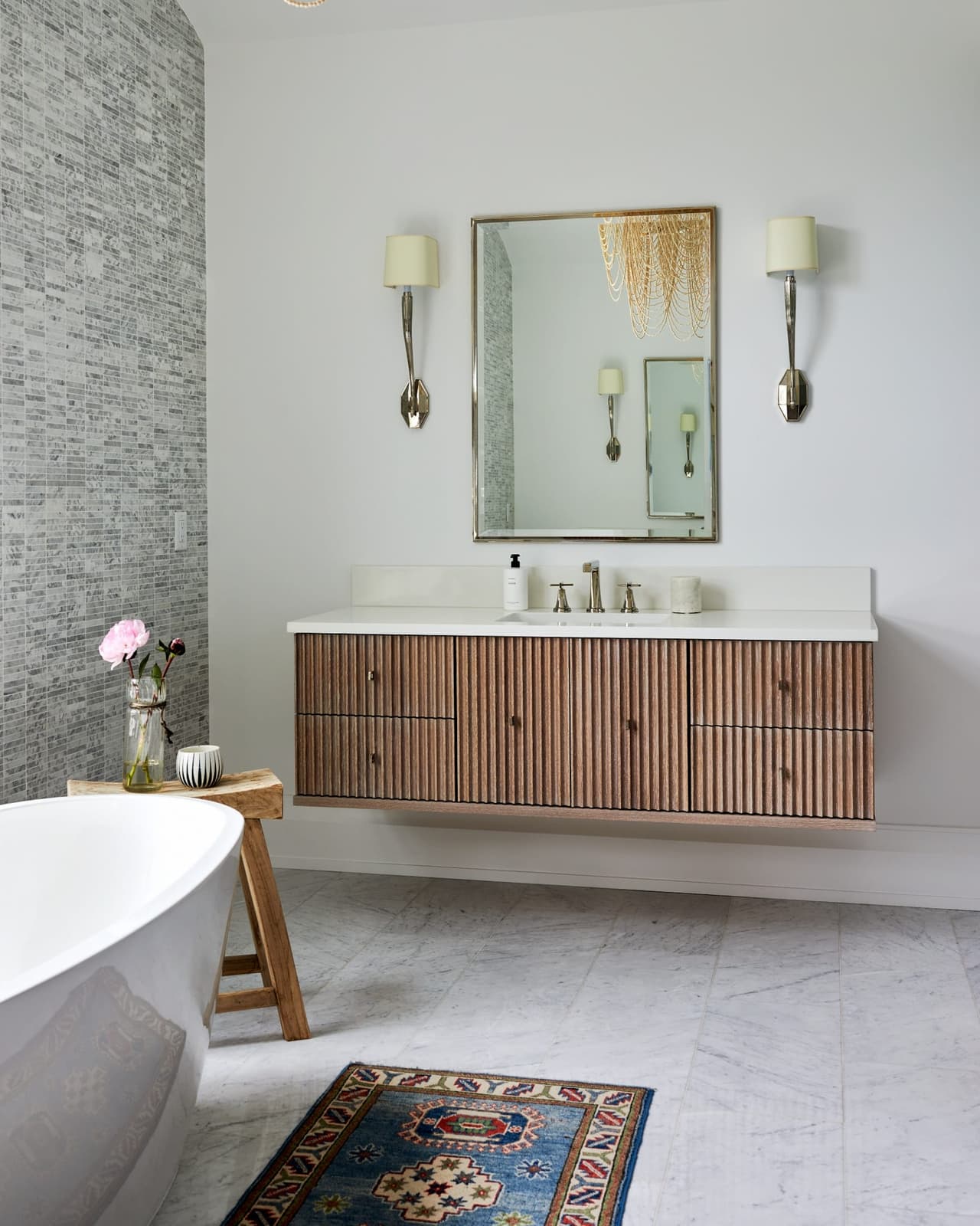 Primary bathroom in a Westfield, NJ new home with a floating fluted wood vanity, a marble top, brass sconces either side of the mirror and the tub beyond, built by Michael Robert Construction