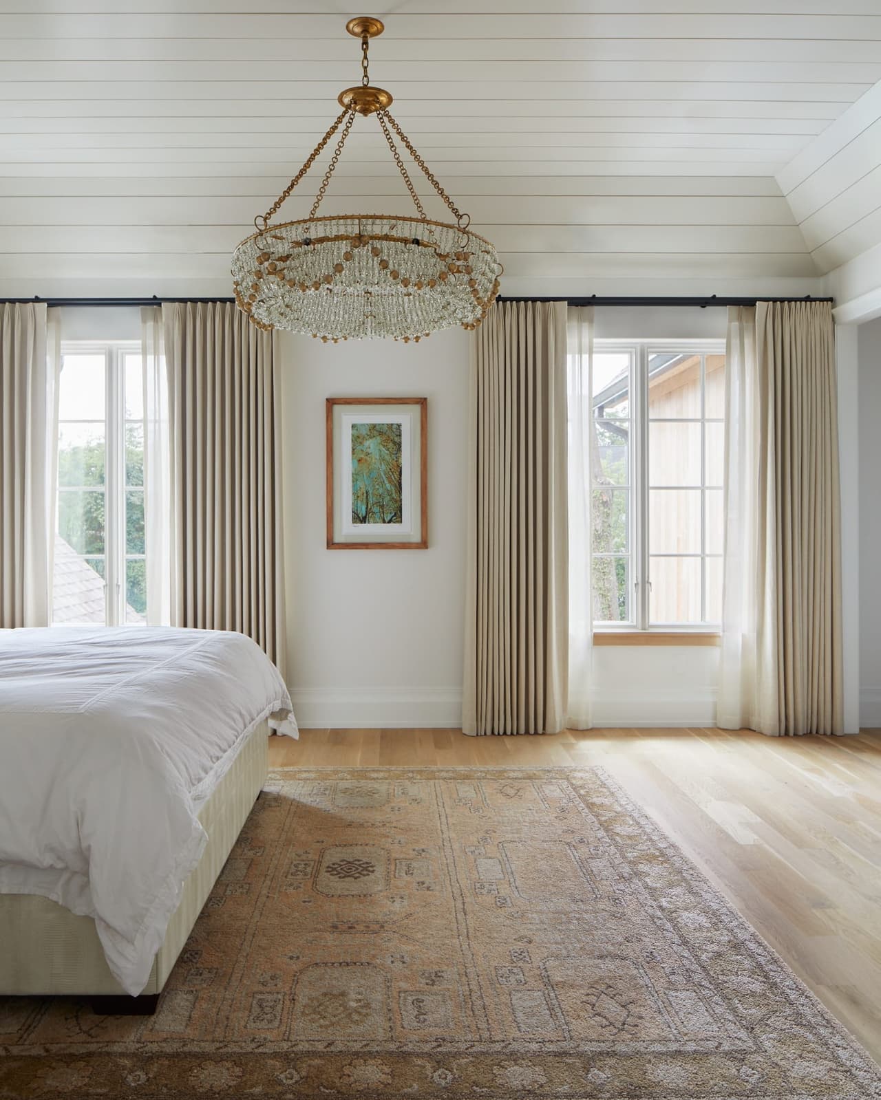 Primary bedroom in a Westfield, NJ custom home, with a beaded chandelier, linen curtains at two windows and an antique rug on wide-plank oak