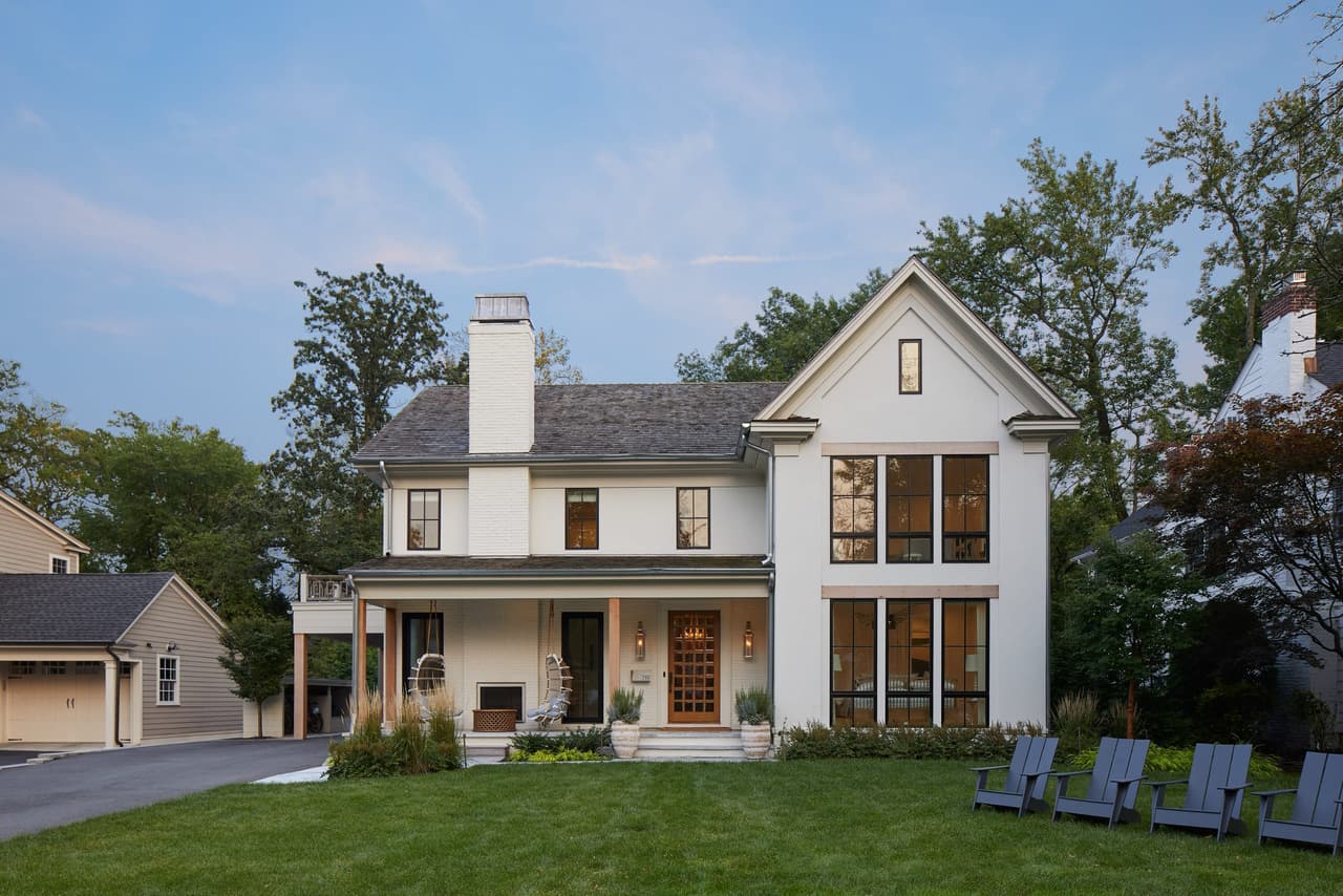 Front of a white modern Tudor new-construction home in Westfield, NJ, with a steep center gable, dark window frames and a covered porch, built by Michael Robert Construction