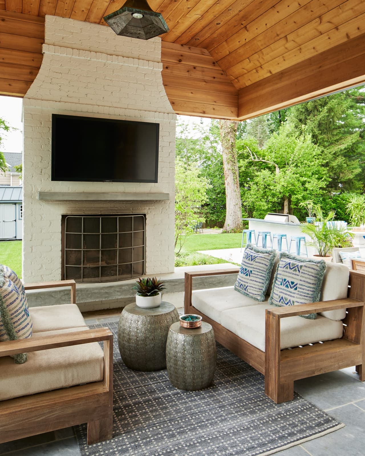 Covered pergola with a stone fireplace, a wall-mounted television and cushioned seating in Westfield, NJ