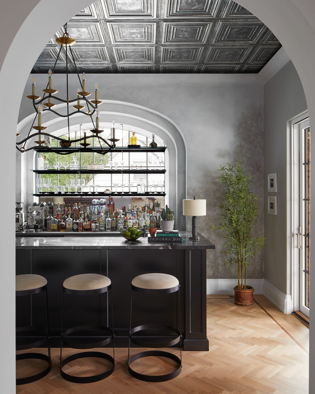 Arched opening into the pub of a Westfield, NJ new-construction home, framing the back bar and its steel window under a pressed-tin ceiling
