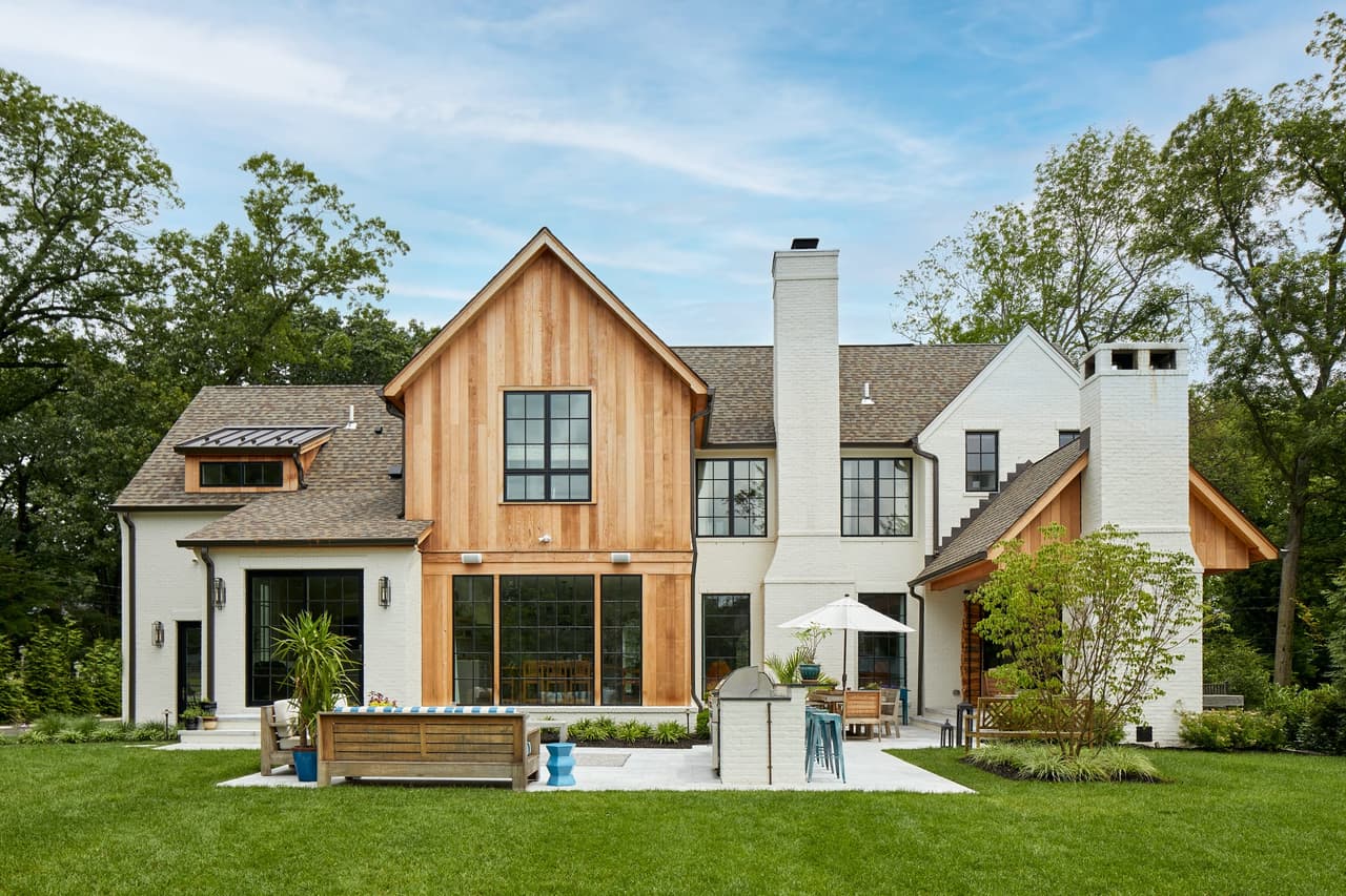 Rear exterior of a Westfield, NJ new home with a cedar-clad center gable between white painted sections, tall chimneys and a run of lawn, built by Michael Robert Construction