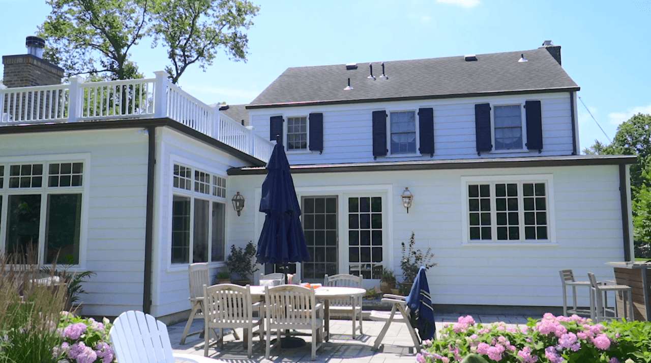 Backyard of a Westfield, NJ remodel and addition, with a paver terrace, teak dining chairs, a deck above and hydrangeas along the border