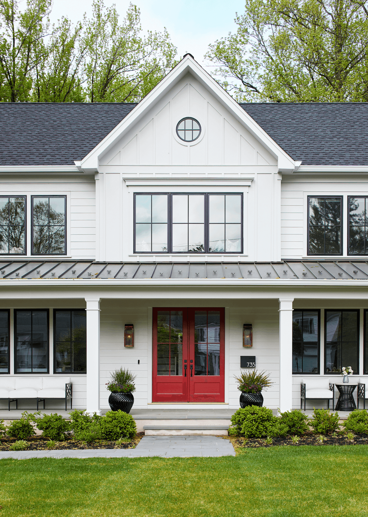 Front porch of a white board-and-batten modern farmhouse with a red double front door, black windows and a standing-seam porch roof in Westfield, NJ