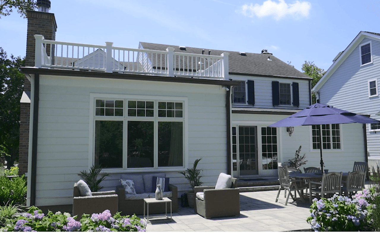 Rear elevation with a second-floor deck above a patio with outdoor seating and an umbrella, in Westfield, NJ