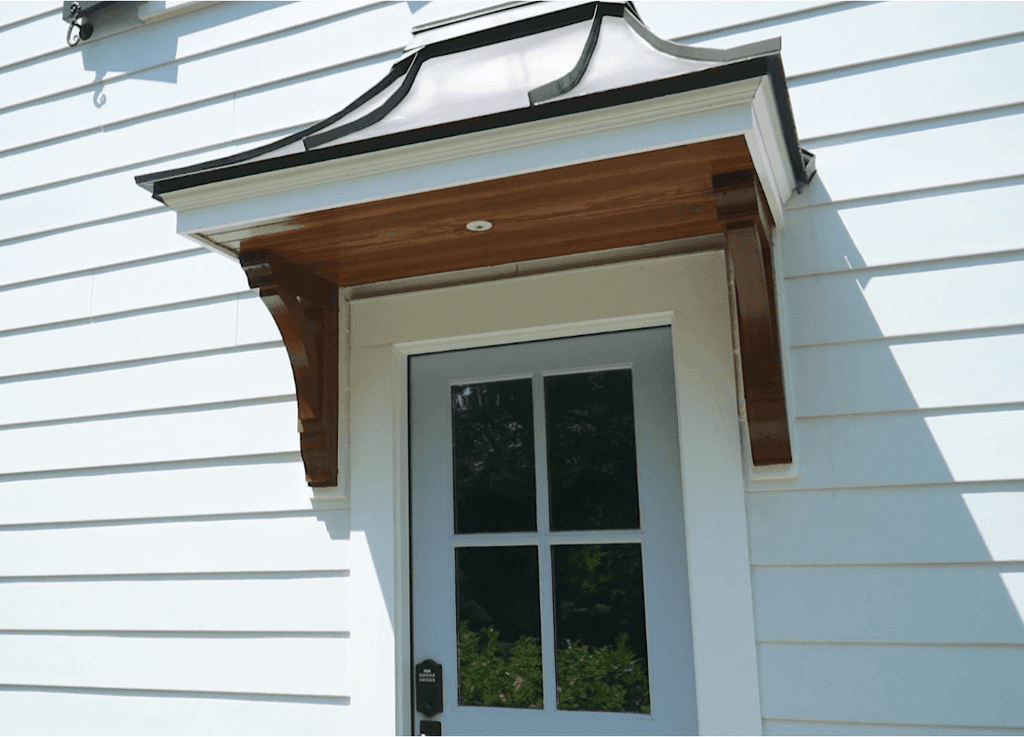 Bracketed bell-curved hood over a side door on the clapboard of a Westfield, NJ remodel and addition, lined in stained wood underneath